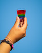 Isolated hand holding a rainbow jello shot with blue background
