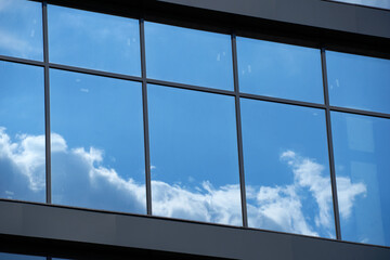 facade of a modern building on a bright Sunny day, blue sky and clouds reflecting in a glass, beautiful exterior of the new building