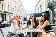 © Vadim Pastuh - Young girls spend their leisure time in a cafe on the summer terrace. Three attractive young women sit at an outdoor table and make selfies together.