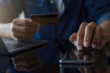 Wall Mural - Man paying and shopping by using credit card and mobile smart phone with laptop computer and calculator on the desk at home office. e business concept.