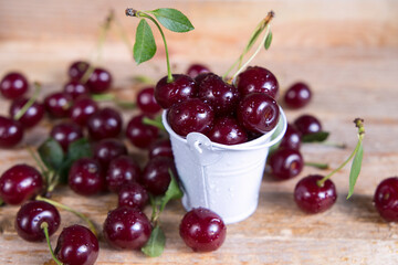 Wall Mural - Cherry with leaves in a mini bucket on a wooden table.