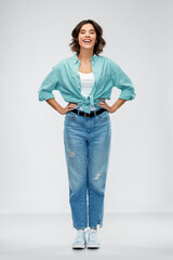 people concept - portrait of happy smiling young woman in turquoise shirt and jeans over grey background