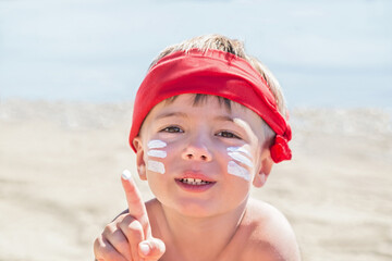 Wall Mural - Sunscreen (suntan lotion) is on hipster boy face before tanning during summer holiday on beach. Caucasian child (kid) is smiling in sunny day (not far from Trieste, Italy).