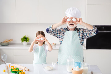 Sticker - Portrait of nice cheerful kind grey-haired grandparent grandchild cooking homemade domestic dough cookery having fun leisure eggs like glasses at modern light white interior kitchen house