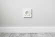 New electrical socket isolated on gray wall. Renovated studio apartment power supply background. Gray wooden floor. Empty copy space white plastic power outlet.