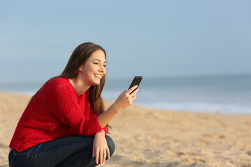 Wall Mural - Happy woman in red checking smart phone on the beach