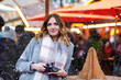 Beautiful young woman drinking hot punch, mulled wine on German Christmas market. Happy girl in winter clothes with lights on background on winter snow day in Berlin, Germany.
