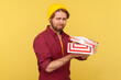 © khosrork - Upset hipster guy in beanie hat and checkered shirt holding opened gift box, looking at camera unhappy disappointed, dissatisfied with awful birthday present. studio shot isolated on yellow background