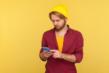Wall Mural - hipster trendy guy in beanie hat and checkered shirt using cell phone, texting or reading message, c
