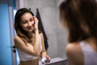 © dianagrytsku - Portrait of young asian woman applying moisturizer cream on her pretty face and look mirror.