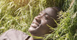 © Prostock-studio - Cheerful african american man lying on green grass at park