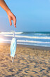 © Fostock12 - Woman's hand dropping coronavirus protective face mask on the beach.
