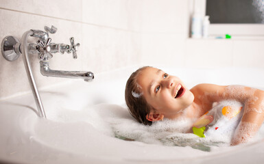 Funny little girl bathes in a bathtub with an inflatable lifebuoy