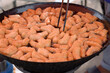 Many deep-fried doughstick are in a large iron pan, With boiling oil.