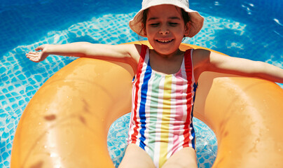 Kid in a colorful swimming suit relaxing on an inflatable ring floating in a pool having fun during summer vacation. Happy cute little girl lying on an inflatable circle in the swimming pool.