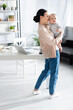 © LIGHTFIELD STUDIOS - attractive mother standing and holding in arms cute infant son in baby romper near gadgets on table