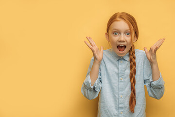 portrait of surprised caucasian girl with natural red hair, isolated over yellow background. happy girl surprisingly react on news, stand with opened mouth and arms up