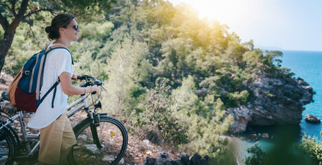 Female with a bicycle by the sea on a hill, summer vacation and travel by bicycle, sports and outdoor activities