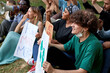 © Roman - young caucasian and african american people sit on grass int he park with placards and chant slogans to demand an action on climate change