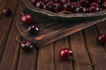 Fresh organic red cherry fruits in a vintage silver plate on a wooden textured old cutting board on a table of wooden boards