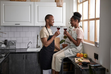 cute lovely dark-skinned couple with glass of wine in the kitchen, spend weekends together, after cooking