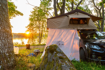 suv with a roof top tent at sunset by a lake in sweden