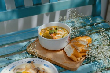 High angle closeup shot of a soup with seafood and vegetables with baguette slices on a blue bench