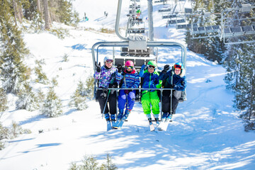 Children in bright ski outfit wave hands sitting on the chairlift happy lifting on the mountain