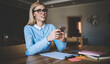 © BullRun - Successful female student in optical spectacles holding smartphone gadget in hands for making research of information for design course work, woman studying in college campus during free time