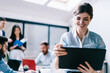 © BullRun - Cheerful young woman in formal wear watching funny video on website on modern touch pad device using wireless internet.Positive female employee reading news on tablet during brainstorming