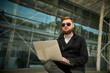 © Volodymyr - Manager holding laptop, Out of office work, young businessman in sunglasses using computer for his job at outside. Handsome bearded hipster, Communication and technology, in the open air, Surfing