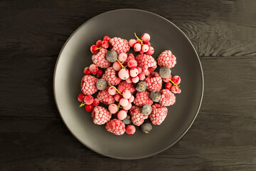Wall Mural - Frozen berries  in the black plate in the center of  the black wooden background. Top view. Copy space.