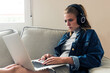 © JAKE JAKAB/ADDICTIVE STOCK - Focused young female freelancer in casual wear with wireless headphones sitting on sofa and using laptop while working on remote project at home