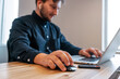 © JAKE JAKAB/ADDICTIVE STOCK - male entrepreneur sitting at wooden table in creative workspace and working on remote project while using netbook