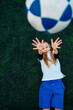 © JOSE LUIS CARRASCOSA/ADDICTIVE STOCK - From above joyful preteen girl in white and blue uniform throwing soccer ball while lying alone on green field in modern sports club