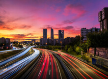 Drone View Of Cityscape With Luminous Highway In Long Exposure And Skyscrapers Under Sunset Sky