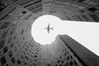 © Juan Lopez/ADDICTIVE STOCK - From below of black and white aircraft flying high over modern building with round yard in in city
