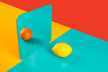 Vibrant Background With Mirror Reflection Of Fresh Orange As Lemon On Blue Surface In Composition With Empty Red And Yellow Areas Like Concept Of Perception In Three Dimensional Space And Distortion Of Imagination