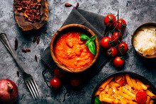 From Above Colorful Arrabiata Sauce In Wooden Bowl Decorated With Fresh Basil Near Fresh Cherry Tomatoes And Bowls With Cheese And Sun Dried Tomatoes And Fresh Delicious Pasta Decorated With Ripe Cherry Tomatoes On Shabby Table With Grey Napkin