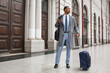© Widetape/ADDICTIVE STOCK - Handsome African-American businessman in trendy elegant suit and coat standing with suitcase