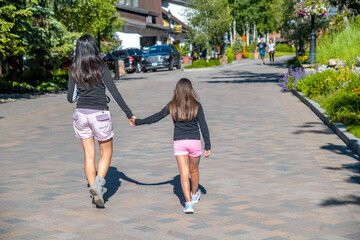 Canvas Print - Woman with her daughter walking in a beautiful mountain town, back view