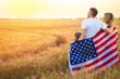 © ZaStock - Back view of a unrecognizable Happy family in wheat field with USA, american flag on back.
