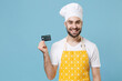 Smiling young bearded male chef or cook baker man in apron white t-shirt toque chefs hat isolated on blue background studio portrait. Cooking food concept. Mock up copy space. Hold credit bank card.