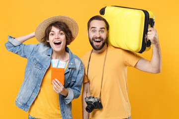 Excited young tourists couple friends guy girl in summer clothes hat isolated on yellow background. Passenger traveling abroad on weekends. Air flight journey concept. Hold passport tickets suitcase.