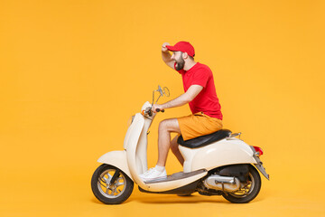 Wall Mural - Delivery man in red cap t-shirt uniform driving moped motorbike scooter isolated on yellow background studio Guy employee working courier Service quarantine pandemic coronavirus virus covid-19 concept