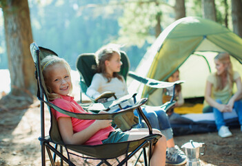 Wall Mural - Smiling girl sitting in chair at campsite