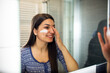 © Novak - Portrait of lady applying cream on face while looking at reflection in bathroom