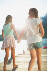 Wall Mural - Sisters holding hands on dock over lake