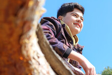 Beautiful Bottom Portrait Of A Smiling Boy With The Sun Against A Blue Sky And Leaning On An Orange Tree Trunk