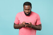 © ViDi Studio - Young african american man guy in casual pink t-shirt isolated on pastel blue wall background studio portrait. People lifestyle concept. Mock up copy space. Using mobile phone, typing sms message.